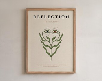 May include: A framed art print with the word "REFLECTION" at the top. Below the title is "THE VISIONARY". The artwork features a stylized plant with two sets of eyes, one green and blue, the other brown and red. The bottom text reads "YOU WERE NEVER LOST, ONLY LOOKING AT YOURSELF THROUGH UNFAMILIAR EYES."