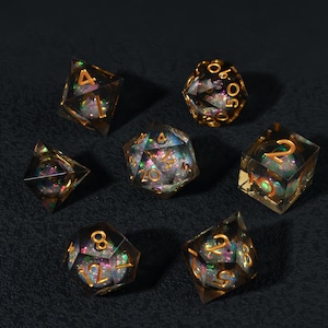 May include: A set of seven polyhedral dice for tabletop games. The dice are clear with iridescent glitter and gold-colored numbering. The dice are arranged on a dark, textured surface.