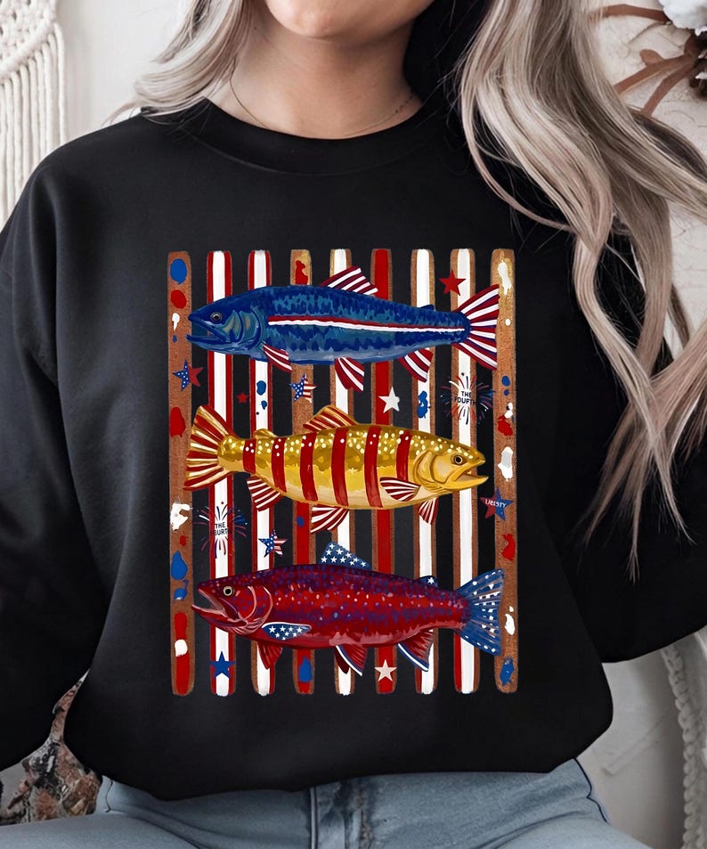 May include: A black crewneck sweatshirt featuring a graphic print of three fish layered over vertical red, white, and blue stripes. The top fish is blue, the middle is yellow, and the bottom is red, all accented with star and firework motifs.