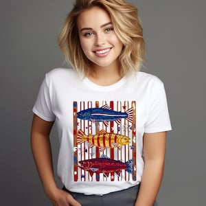 May include: A white short-sleeved t-shirt featuring a graphic print of three fish stacked vertically. The fish are colored in shades of blue, yellow, and red, set against a background of vertical brown stripes and small star accents.