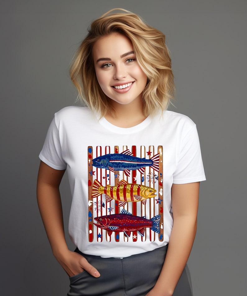May include: A white short-sleeved t-shirt featuring a graphic print of three fish stacked vertically. The fish are colored in shades of blue, yellow, and red, set against a background of vertical brown stripes and small star accents.