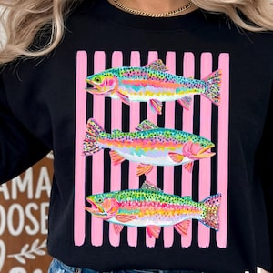 May include: A black long-sleeve sweatshirt featuring a graphic print of three colorful rainbow trout fish layered over a background of vertical pink and black stripes. The fish are depicted in vibrant shades of green, pink, yellow, and blue.