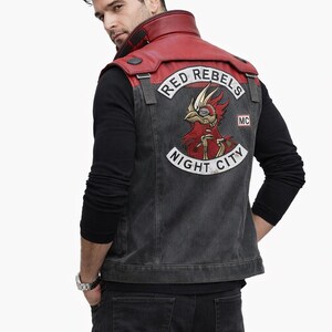 May include: A denim vest with a red leather collar and a graphic patch that reads "RED REBELS NIGHT CITY MC". The vest is worn over a black long-sleeve shirt and paired with black jeans. The image is set against a white background.