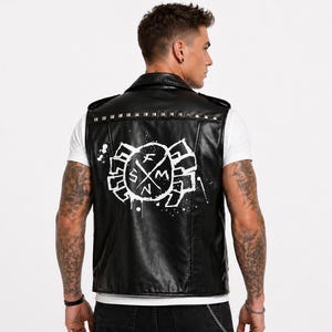 Pu&ograve; includere: Gilet in pelle nera con borchie argentate sul colletto. La parte posteriore presenta un design grafico bianco con le lettere "SFM" e una croce. Il gilet &egrave; indossato sopra una maglietta bianca.