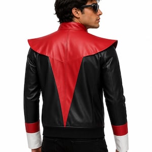 May include: A black and red jacket featuring a high collar and a prominent red V-shaped panel on the back. The sleeves have red and white cuffs, and the hem is finished with a black ribbed band. The jacket is constructed from smooth material.