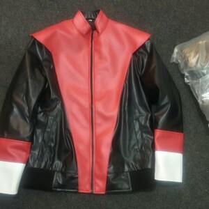 May include: A black jacket featuring a red V-shaped panel on the front, a high collar, and a full-length front zipper. The sleeves have red and white bands at the cuffs, and the bottom hem is finished with a black ribbed waistband.