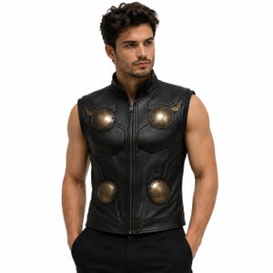 May include: A black sleeveless vest featuring a high collar, a full-length front zipper, and four prominent circular metallic bronze-toned discs positioned on the chest and waist areas, mimicking a superhero-inspired armor design.