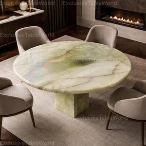 May include: A round, green and white marble dining table with a square base. The table is surrounded by four beige upholstered chairs. The table is approximately 152 cm in diameter.