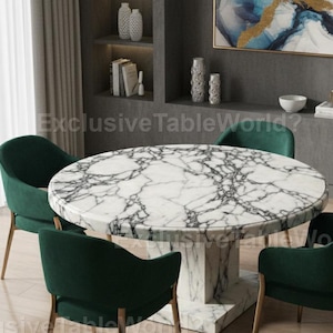 May include: A circular marble dining table with a white base and dark veining. Four green velvet chairs with wooden legs are positioned around the table. The room has a modern design with neutral colours.