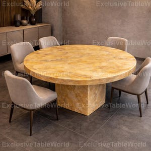 May include: A circular dining table with a golden marble surface and a square pedestal base. Four beige upholstered chairs with dark wooden legs surround the table. The room has a neutral colour scheme and is well-lit.