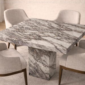 May include: A square marble dining table with a grey and white veined pattern. The table has a thick, solid base and is surrounded by four upholstered chairs with wooden legs. The chairs are a light beige colour.