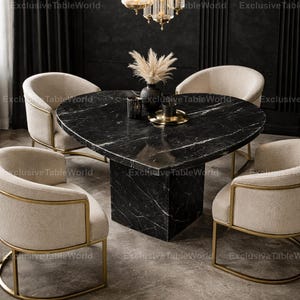 May include: A black marble dining table with a heart-shaped top and a solid base. Four cream armchairs with gold frames are arranged around the table. A vase with pampas grass and candles decorates the table's surface.