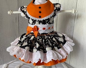 Pode incluir: Um vestido preto e branco com estampa de fantasma e acabamento laranja. O vestido tem uma borda de renda branca e um babado branco na parte inferior. O vestido está em um manequim branco.