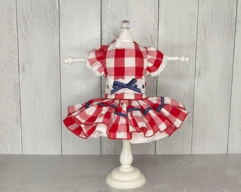 May include: Red and white gingham dog dress with a blue and white polka dot bow and blue trim. The dress is on a white mannequin.