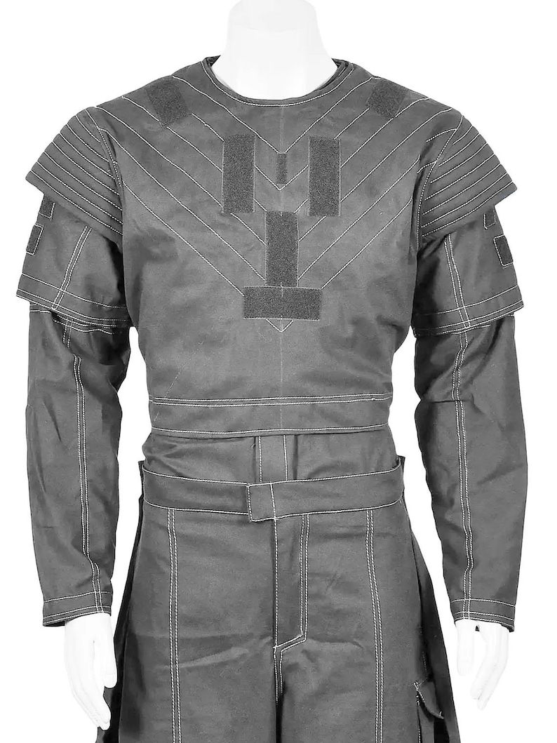 May include: A gray uniform with white stitching, featuring a long-sleeved top with shoulder pads and a matching pair of pants. The top has a chevron design and several rectangular patches. The pants have a belt and pockets.