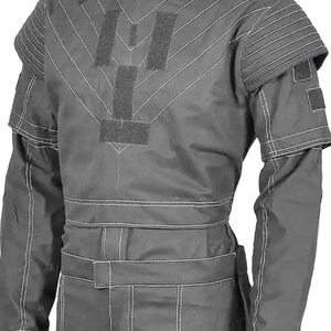May include: A gray protective suit with white stitching and multiple Velcro patches. The suit features a round neck, long sleeves, and a belt. The shoulders have padded sections, and the suit appears to be made of a durable material.