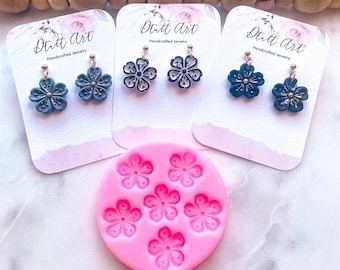 May include: Blue and gold floral earrings, handcrafted and displayed on cards with the text "Ditt Art". A pink silicone mould with flower shapes is also visible. The earrings are a delicate accessory.