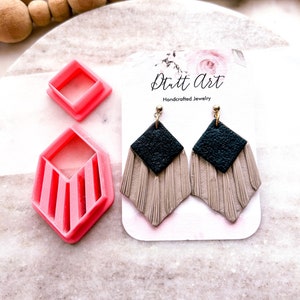 May include: A pair of handmade earrings with a black and beige tassel design. The earrings are displayed on a white card with the text "Dritt Art Handcrafted Jewelry".