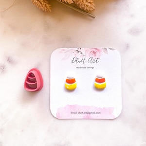 Puede incluir: Un par de pendientes de maíz dulce hechos a mano en una tarjeta blanca con el texto "Dutt Art Handmade Earrings" y la dirección de correo electrónico "dutt.art@gmail.com".