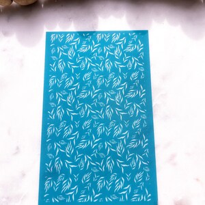 May include: A blue stencil with a white leaf pattern. The stencil is rectangular and has a smooth surface.