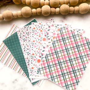 Pode incluir: Cinco folhas de papel com diferentes padrões, incluindo xadrez rosa e verde, flores rosa e verde e listras rosa e verde.
