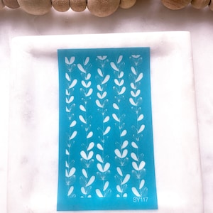 May include: A blue stencil with a white design of leaves and branches. The stencil has the text "SY117" in the bottom right corner.