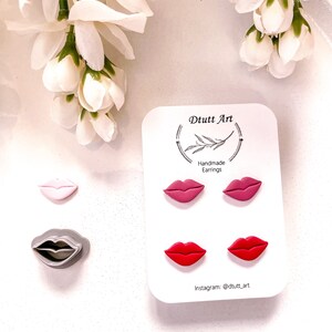 Peut inclure: Un ensemble de trois paires de boucles d'oreilles en argile polymère faites à la main en forme de lèvres. Les boucles d'oreilles sont en rose, rouge et gris. La carte indique "Dtutt Art Handmade Earrings" et "Instagram: @dtutt_art".