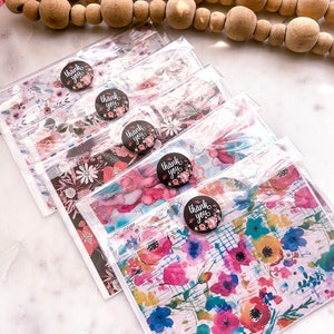 May include: Five thank you cards with floral designs and black and white "Thank You" stickers. The cards are packaged in clear plastic sleeves.