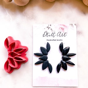 May include: A pair of black statement earrings with a floral design. The earrings are handcrafted and are displayed on a white card with the text "Dutt Art Handcrafted Jewelry".