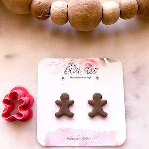 May include: A pair of brown gingerbread man-shaped polymer clay earrings on a white card with the text "Dutt Art Handmade Earrings" and "Instagram: @dutt_art".