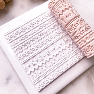 Könnte beinhalten: Ein rosa Nudelholz mit einem erhabenen Design aus geometrischen Mustern. Das Nudelholz liegt auf einer weißen Silikonmatte mit dem gleichen Design, das in die Oberfläche geprägt ist.