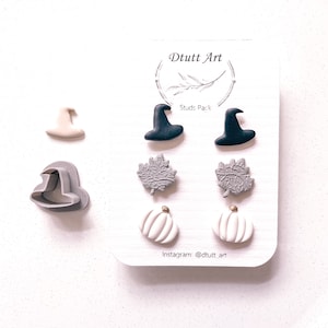May include: A set of six Halloween-themed earrings, including witch hats, pumpkins, and leaves. The earrings are made of polymer clay and come in black, white, and gray colors. The card reads "Dtuutt Art" and "Studs Pack".