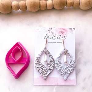 May include: White floral dangle earrings with a pearl accent. The earrings are on a white card with the text "Dritt Art Handcrafted Jewelry".