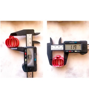 May include: Two red plastic pumpkin cookie cutters are measured with a digital caliper. The larger cutter measures 1.96 inches and the smaller cutter measures 1.19 inches.