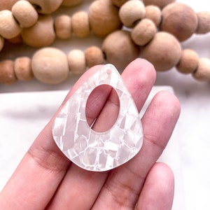 May include: White, opaque, teardrop-shaped earring with a textured, marbled finish and a hole at the top for hanging.