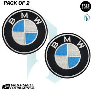 May include: Two circular black embroidered patches with the BMW logo. The logo features a blue and white quadrant design within a black ring, with the letters "B", "M", and "W" in white. The text "PACK OF 2" is at the top.