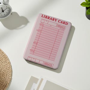 May include: A pink rectangular item with the words "LIBRARY CARD" in red. The item has a grid of lines and boxes, resembling a library card. A white alarm clock and a small potted plant are also visible.