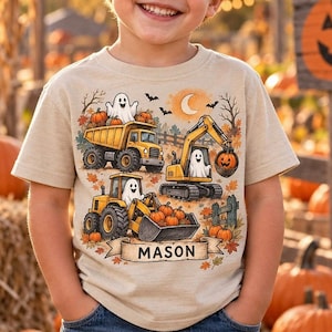 May include: A beige short-sleeve t-shirt featuring a graphic print of yellow construction vehicles, including a dump truck, excavator, and tractor, operated by white ghosts. The design includes pumpkins, autumn leaves, and a banner with the name MASON.