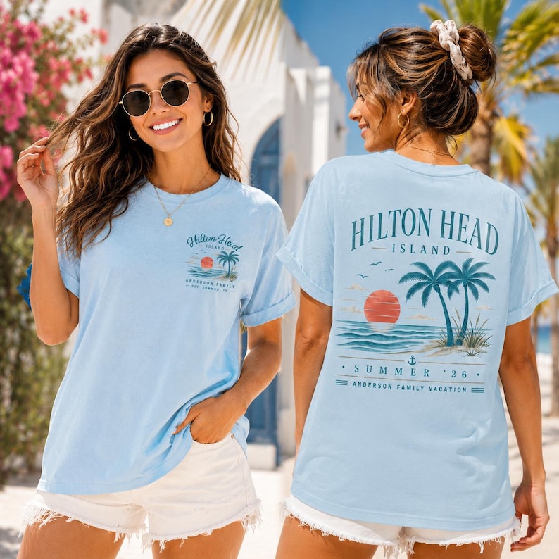 May include: A light blue short-sleeve t-shirt featuring a small graphic on the front left chest and a large graphic on the back. Both graphics depict a sunset over the ocean with palm trees and the text Hilton Head Island Summer '26.
