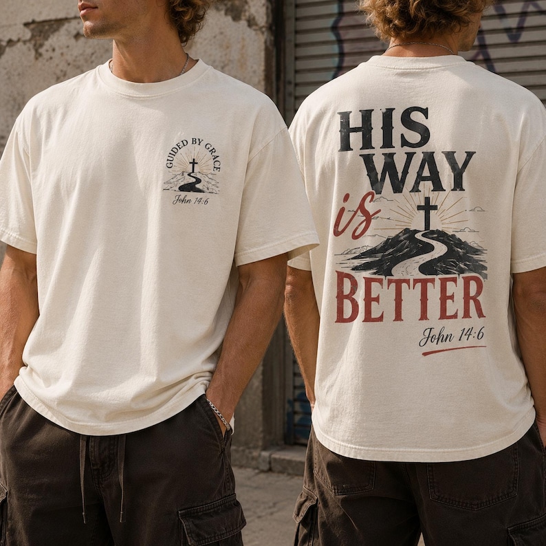 May include: An off-white short-sleeve t-shirt featuring a small graphic on the front chest with a cross, a winding path, and the text "Guided by Grace John 14:6". The back displays a large graphic with the text "HIS WAY is BETTER" and a cross.
