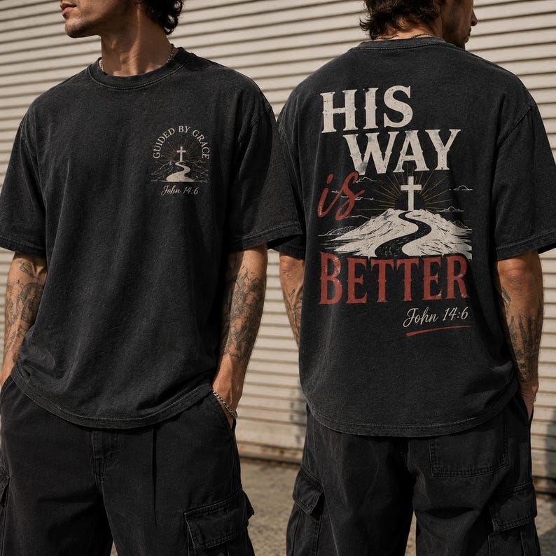 May include: A black short-sleeve t-shirt featuring a small graphic on the front chest with a cross and the text "GUIDED BY GRACE John 14:6". The back displays a large graphic with the text "HIS WAY is BETTER" and "John 14:6" above a cross.