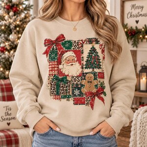 May include: A beige crewneck sweatshirt featuring a patchwork-style graphic print. The design includes a central image of Santa Claus, a decorated Christmas tree, a gingerbread man, gift boxes, and red bows, all accented with plaid and leopard patterns.