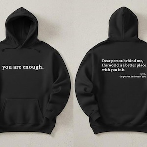 May include: Black hoodie with the phrase "you are enough" printed on the front. The back of the hoodie has the text "Dear person behind me, the world is a better place with you in it, love, the person in front of you."