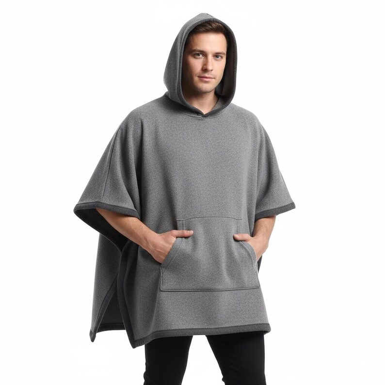 May include: A gray hooded poncho with a kangaroo pocket. The poncho has dark gray trim around the hood, sleeves, and bottom. The person is wearing black pants. The poncho is made of a soft, warm material.