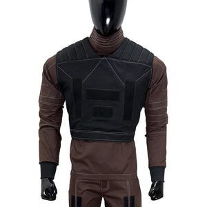 May include: A black tactical vest with multiple velcro patches is displayed on a mannequin. The vest is worn over a brown long-sleeved shirt and matching pants. White stitching details the vest and clothing. The mannequin has a black head and hands.