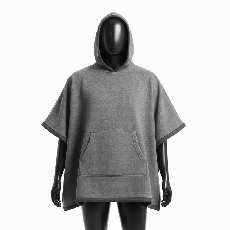 May include: A gray hooded poncho with a kangaroo pocket, displayed on a black mannequin. The poncho has a textured surface and dark gray trim around the hood, sleeves, and pocket. The garment is designed for comfort and casual wear.