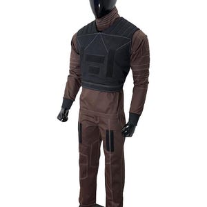 May include: A brown jumpsuit with a black vest, displayed on a mannequin. The jumpsuit has white stitching and black patches on the legs. The vest has a geometric design with black patches. The mannequin has a black head and hands.