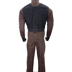 May include: Brown jumpsuit with a black vest, displayed on a mannequin. The jumpsuit has white stitching and geometric patterns on the sleeves. The black vest has white stitching. The mannequin has a black head.