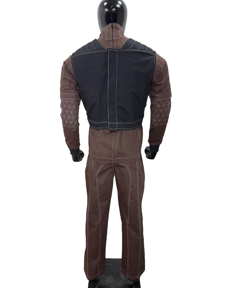 May include: Brown jumpsuit with a black vest, displayed on a mannequin. The jumpsuit has white stitching and geometric patterns on the sleeves. The black vest has white stitching. The mannequin has a black head.