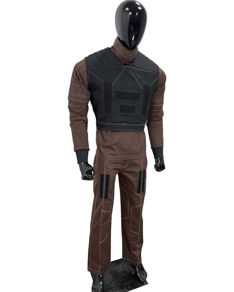 May include: A brown tactical outfit displayed on a mannequin. The outfit includes a black vest with multiple panels, a long-sleeved shirt, and matching pants. The pants have black patches and white stitching. The mannequin has a black head and gloves.